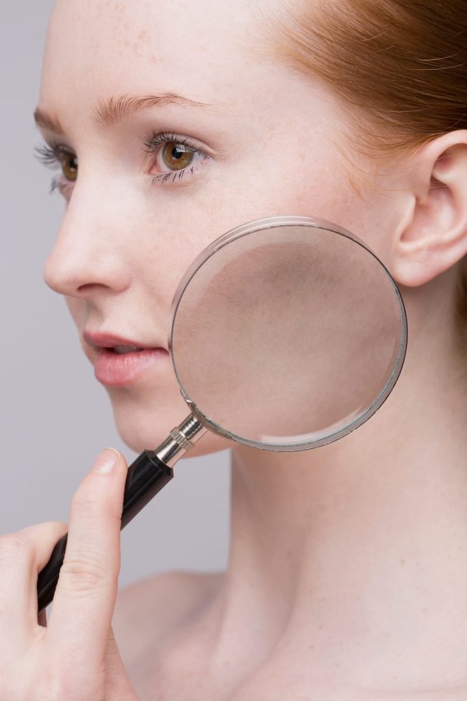 Woman examining her skin with a magnifying glass